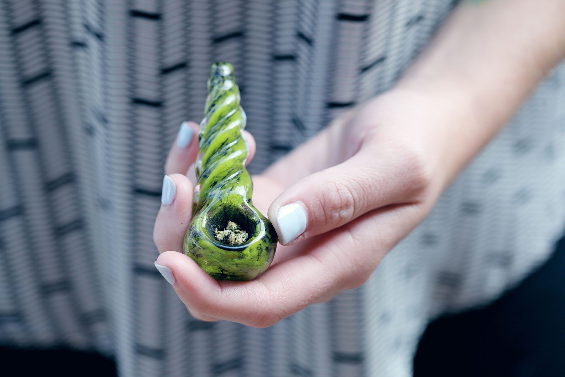 woman's hand holding a cannabis pipe with flower in it