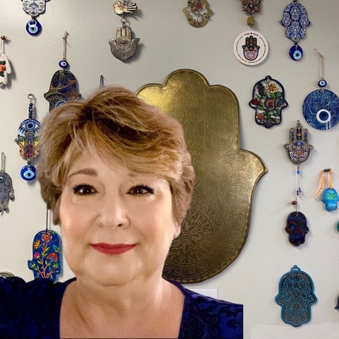 Stephanie Kahn in front of a wall displaying a large hamsa collection at Takoma Wellness Center.