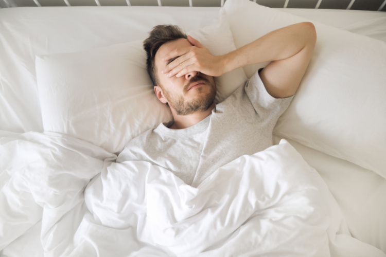 Person lying awake in bed with a hand over their face
